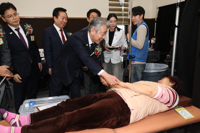 강호동 농협중앙회장이 환자용 침대에 누워있는 농업인의 손을 따뜻하게 맞잡고 있다.